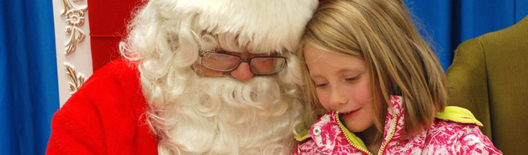 Young girl sitting on Santa's lap and reading her Christmas list